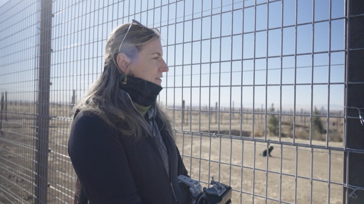 Woman holding a radio controller beside a tall wire fence